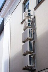 Multiple air conditioning units mounted on a building wall in a sunny urban environment