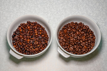 Comparison of roasted coffee beans in white plates on a table. Different sizes and qualities of whole coffee beans