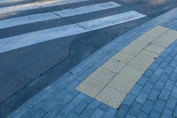 A crosswalk is visible with marked white stripes on a city street, accompanied by textured yellow...