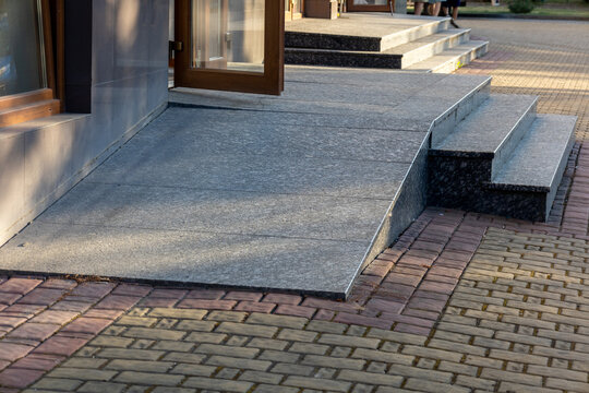 Bright daylight highlights a smooth ramp and steps leading to the entrance of a contemporary building, enhancing accessibility for visitors