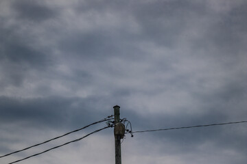 A single weathered utility pole with electrical wires stands against a dramatic, overcast sky filled with moody dark clouds.