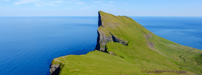 Towering green Mylingur cliff jut dramatically into the tranquil blue sea, showcasing the stunning...
