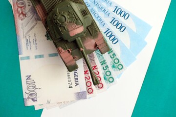 Nigerian naira currency money bills and toy tank on flag. The concept of army funds and weapons sales
