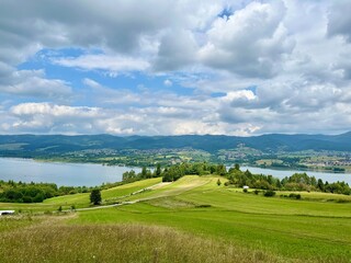 Panoramic summer view of Czorsztynskie lake with green fields and cloudy sky. Concept: eco tourism, scenic travel, outdoor exploration.	