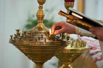A church priest with a Bible in his hands lights a candle on a pedestal