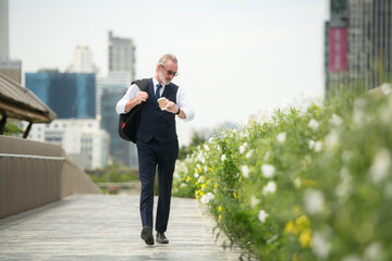 Senior businessman in a suit walking outdoors, checking the time on his watch