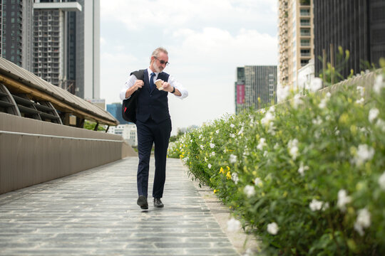 Senior businessman in a suit walking outdoors, checking the time on his watch