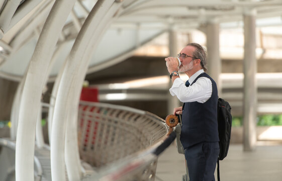Smiling senior businessman holding a coffee cup and electric skateboard