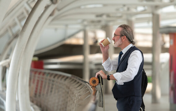 Smiling senior businessman holding a coffee cup and electric skateboard
