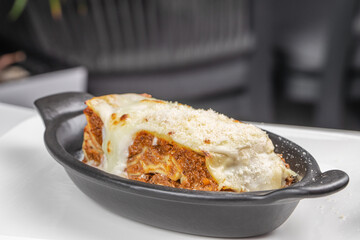 Baked lasagna with melted cheese and meat sauce served in a black ceramic dish