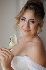 Elegant bride holding a white rose in a soft-lit indoor setting before her wedding ceremony