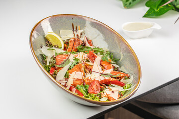 Fresh salmon salad with parmesan, arugula, and tomatoes served with lemon and dressing