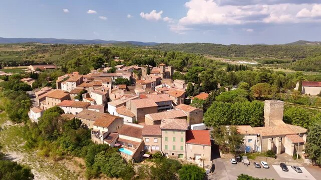 Aerial view of the village of Agel, France, nested in the hills of Occitanie, with traditional terracotta colored houses and a castle, surrounded by vineyards and forests.