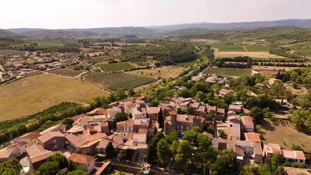 Aerial view of the village of Agel, France, nested in the hills of Occitanie, with traditional terracotta colored houses and a castle, surrounded by vineyards and forests.