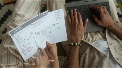 High angle cropped shot of hands of unrecognizable couple looking at utility bills and paying them online using laptop, managing home budget together - Powered by Adobe