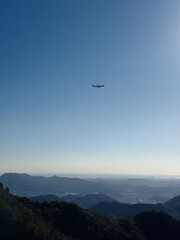 airplane in blue cloudless sky flying over green mountains