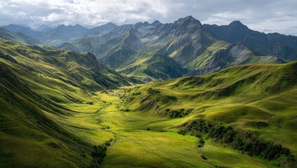 Naklejka premium Sunlit green valley nestled between imposing, sun-dappled mountains under a partly cloudy sky. Rolling hills and a winding stream or river are visible in the valley floor