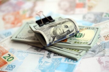 Bunch of US dollar bills lies on big amount of Brazilian reais banknotes close up