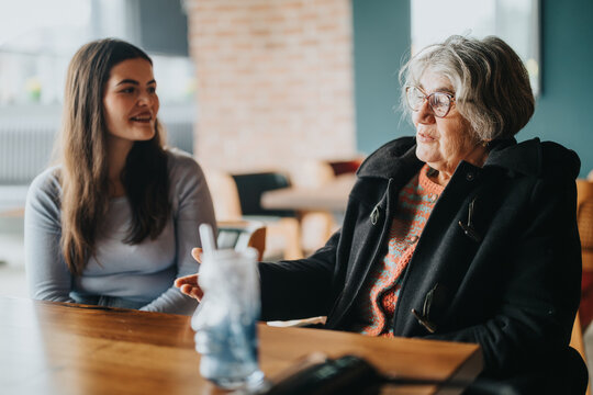A friendly interaction between an elderly woman and a young woman sharing a laugh in a casual cafe environment, showcasing generational connection, dialogue, and warm interactions.