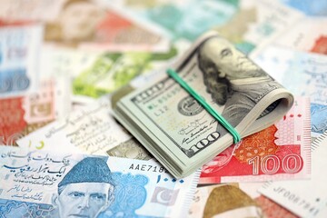 Stack of US dollar bills lies on big amount of Pakistan rupees banknotes close up