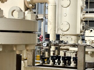 This close-up image reveals a complex arrangement of industrial pipes, valves, and pressure regulators. The machinery, painted in a neutral tone, highlights a detailed segment of a larger factory or p