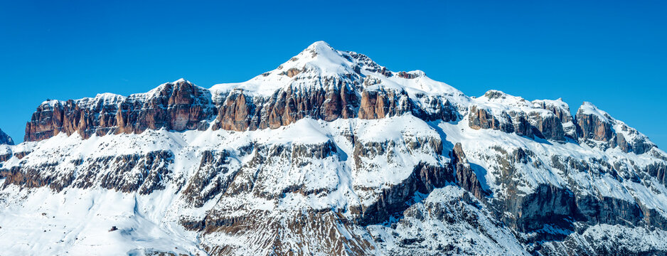 Sella group mountain massif and mountain range in Dolomites in Italy in winter, partially covered with snow. Panoramic view from the South. Famous ski region with many popular resorts around