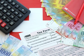 Swiss franc banknotes and tax form with pen. The current francs money bills lies on tax return form