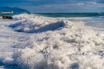 Gelendzhik resort. Large green storm waves in white foam roll over rocky beach of Gelendzhik. Large stones on shore. Splashes and foam from waves
