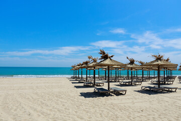 Empty beach with parasols and chaise longues by the sea at resort on sunny summer day