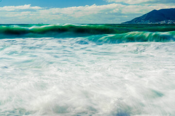 Kabardinka resort. Black sea. Large emerald-colored storm waves. Lots of squirts and foam. Port of Novorossiysk and Caucasus Mountains on horizon. Long exposure photo.
