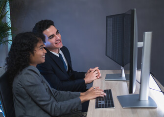 Man and woman team business professional formal attire collaborate desk with dual monitor computer talk about financial stock market in modern office highlight teamwork technology, professional work