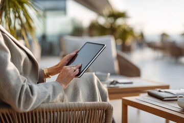 Woman using tablet while relaxing on a terrace at sunset in a modern outdoor setting with comfortable seating