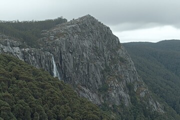 Waterfall cascading down a rugged mountain face, dense forest at base