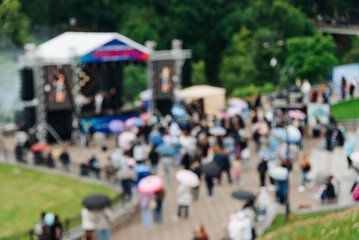 music festival in city park, crowd of people, rock group performing on stage, green trees and summer day, blurred image, background