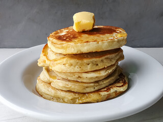 stacked pancakes with butter on a white plate and gray background