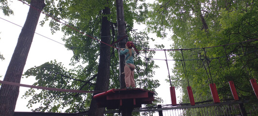 Child balancing on ropes in adventure park among green trees