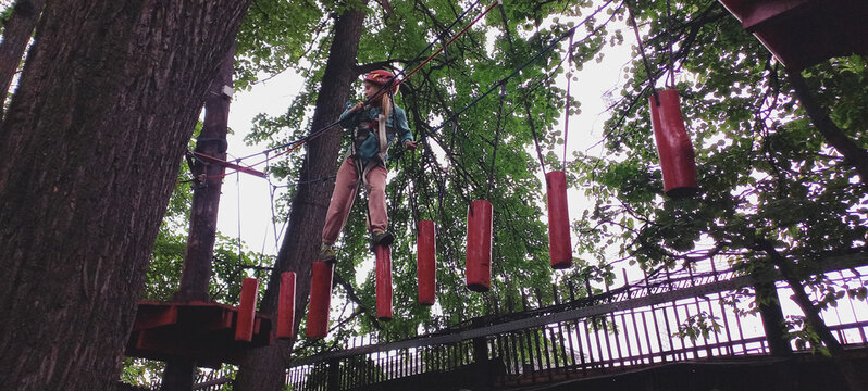 Girl navigating ropes course among trees in adventure park  