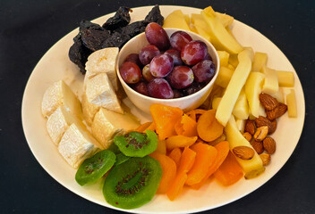 A cheese platter, also known as a cheese board or grazing platter, featuring an assortment of cheeses, fruits (fresh and dried), and nuts. 