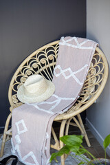 Une chaise en rotin dans un anglet de mur avec dessus un chapeau et une serviette