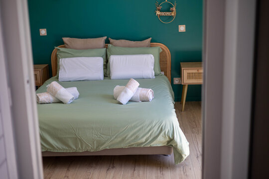 Une chambre dans une villa pour Airbnb, le lit est fait avec des serviettes dessus, la t&ecirc;te de lit et la table de chevet sont en rotin