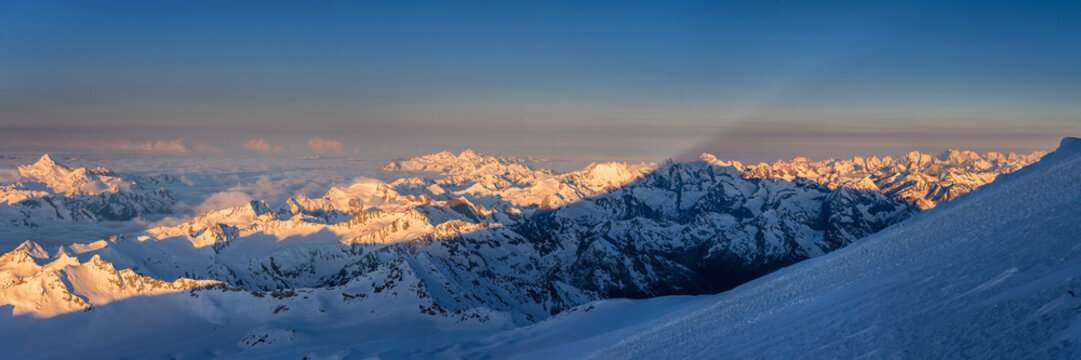 The first rays of the sun illuminate the mountains of the Main Caucasian range. View from the Mt. Elbrus slope in Russia.