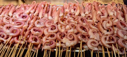 A vibrant display of freshly prepared octopus skewers, showcasing their delicate texture and pinkish hue. © Johari