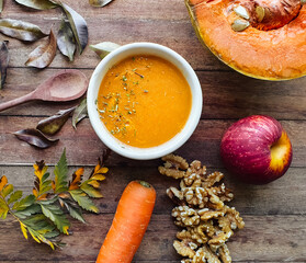 
table with leaves and autumn foods such as pumpkin and carrot cream and spices, apple, nuts on wooden background