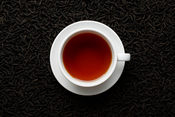 Cup of brewed black loose leaf tea, aromatic traditional beverage on background of dried tea leaves