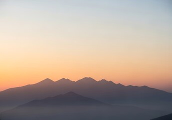 Obraz premium Subtle hues paint the silhouettes of mountains at dusk offering a serene vista