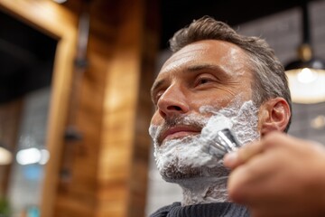 Mature man getting a traditional wet shave with a safety razor at barbershop.