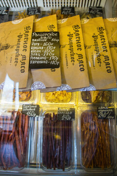 Dried meat and fish snacks with price tags in a Russian market display case. Savory food items for sale.