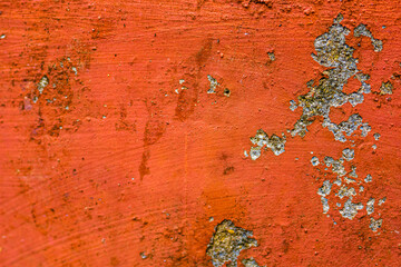 Textured red/orange surface with small peeling patches revealing a gray, rough layer.