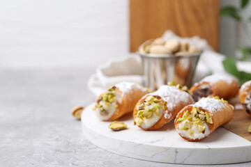 Delicious cannoli with ricotta cheese, pistachios and powdered sugar on grey marble table indoors, closeup. Space for text