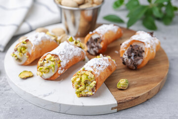 Delicious cannoli with ricotta cheese, pistachios, chocolate and powdered sugar on grey table, closeup